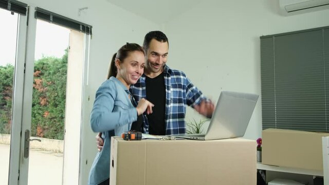 Young couple choosing wall paint color on internet laptop computer for their new house decoration
