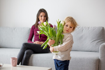 Fototapeta na wymiar Beautiful blond boy, giving mother flowers and box with little gift for mothers day