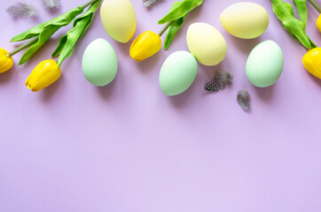 Easter flat lay. Painted eggs with tulips and feathers on lilac background, space for text