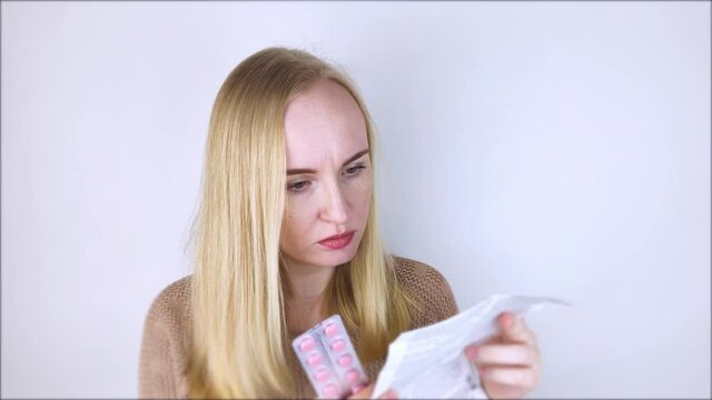 The girl on a white background reads the instructions for medicines. The woman looks at the list and composition of the drug. The concept of home self-medication and the study of the properties of dru