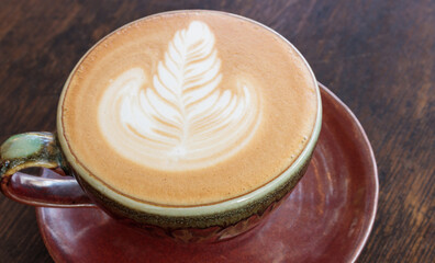 Coffee latte art with tulip shape in a brown cup on old wooden background. Close up photo.