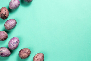 Colorful painted eggs as a border on the turquoise surface. Easter flat lay with copy space.