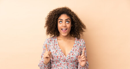 Young African American woman isolated on beige background surprised and pointing up