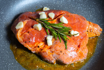 Delicious juicy pork steak seasoned with rosemary and garlic is fried in a pan.