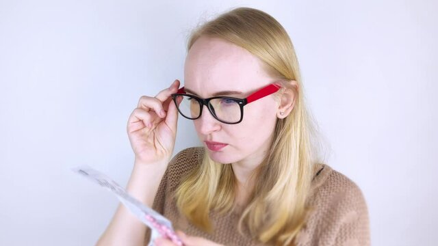 The girl on a white background reads the instructions for medicines. The woman looks at the list and composition of the drug. The concept of home self-medication and the study of the properties of dru