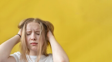 Fototapeta premium one sad girl holding her head in her hands on yellow background. Closed eyes. Teenager problems. Banner. Space for text