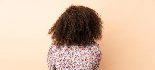 Young African American woman isolated on beige background in back position