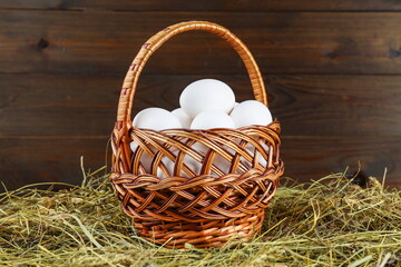 fresh chicken egg basket is on hay on wooden background