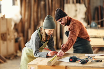 Couple of joiners working with wooden detail in workshop - obrazy, fototapety, plakaty