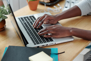 Hands of young woman typing on laptop when working at office desk at home