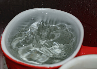 a stream of water pours into a mug with a spoon in the dish sink close-up. blurred focus