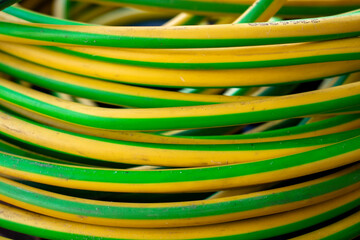 Vibrant yellow and green thick rubberized cables. Close up photo of messy and dirty colorful copper cable wires lying in the garage or storage room.