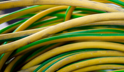 Vibrant yellow and green thick rubberized cables. Close up photo of messy and dirty colorful copper cable wires lying in the garage or storage room.