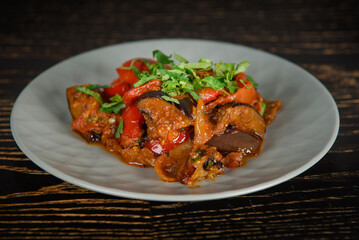 Adjapsandali Georgian dish decorated with herbs on a gray plate on a dark wooden table.