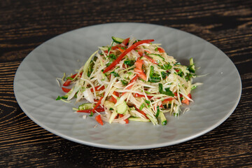 Cabbage, cucumber, tomato, pepper, greens salad on a gray plate on a dark wooden table. Vegetable salad with oil.