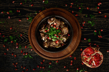 Barbecue meat with onions in a clay plate on a wooden board on a dark wooden table decorated with...