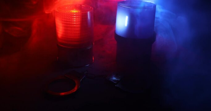 Police raid at night and you are under arrest concept. Silhouette of handcuffs with flashing red and blue police lights at foggy background. Selective focus