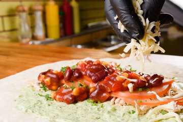Burrito making process. To the meat, the chef adds cheese to beans and corn in tomato sauce, greens...