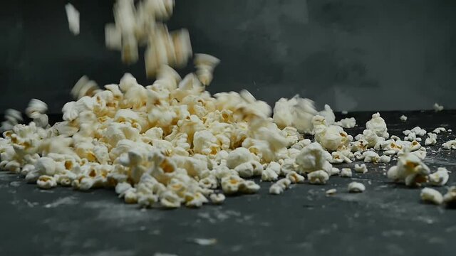 A pile of popcorn poured over a dark gray background. Slow motion. Close-up. Snack while watching a movie