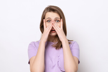 close up scared girl hiding face in palms hands and peering out with one eye between her fingers,...