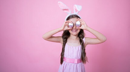 A funny little girl dressed in Easter bunny ears and in a dress posing with Easter eggs copy space.