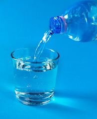 Pouring water from a bottle into a glass in a blue colors design.