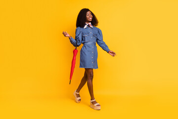 Full length profile photo of gorgeous cheerful dark skin lady hang on arm umbrella isolated on yellow color background