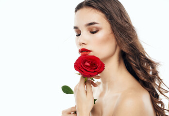 Charming brunette woman with bare shoulders and a fragrant flower near her face