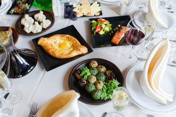 Assortment of dishes phali, khachapuri, salmon, khinkali, vegetables table setting bowl with wine, glasses, dishes, napkins