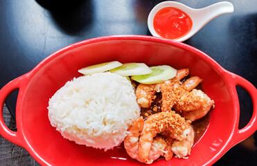 rice with garlic fried shrimp is on a red plate and has chili sauce.