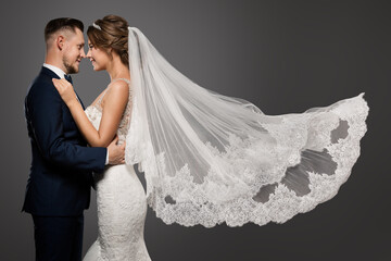 Wedding Couple Dancing. Romantic Bride and Groom Portrait. Bridal long Veil flying over Gray Studio Background