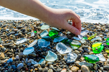 Colorful polished pieces of sea glass collected from the beach in a child hand. Beautiful close-up sea green, blue and white glass on a sea beach background.