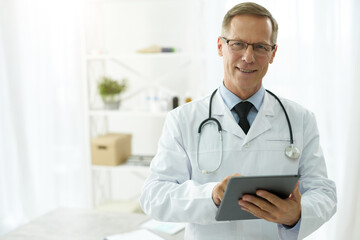 Cheerful doctor in lab coat using tablet computer in clinic