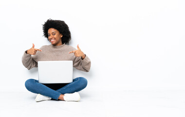 Young African American woman with a laptop sitting on the floor proud and self-satisfied