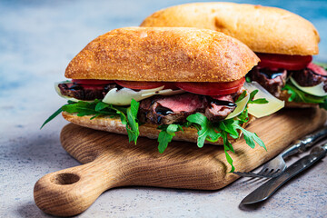 Beef sandwich with arugula, tomato and parmesan on wooden board. Comfort food concept.