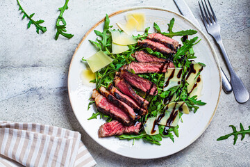 Beef steak tagliata with arugula and parmesan on gray plate, gray background, top view. Italian cuisine concept.