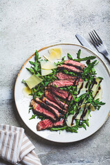 Beef steak tagliata with arugula and parmesan on gray plate, gray background, top view. Italian...