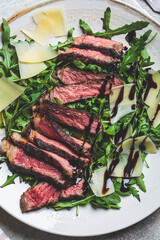 Beef steak tagliata with arugula and parmesan on gray plate, gray background, top view. Italian cuisine concept.