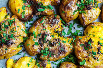 Baked smashed potatoes with herbs on baking sheet, top view, close up.
