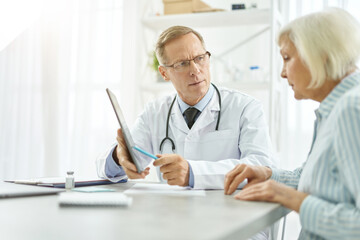 Serious male doctor having appointment with old woman in clinic