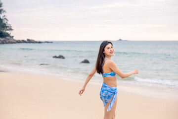 Fototapeta na wymiar Woman with this blue bikini is taking a stroll on the beach happily outdoors at Nai Thon Beach, Phuket, Thailand, the backdrop is blue sea and sky. Concept of truth, travel, happiness, nature