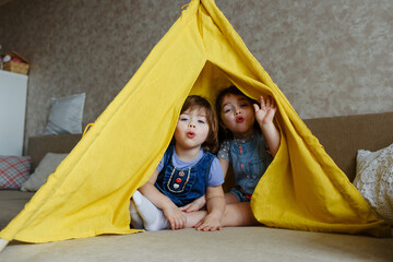 two little girls play at home in yellow in a teepee © Tatsiana