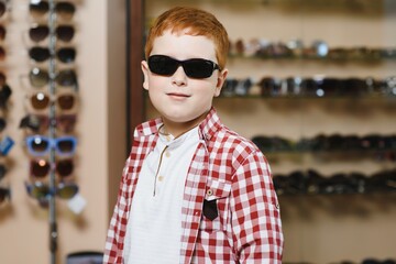 Happy boy choosing sunglasses in optical store.