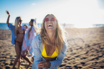 Happy young woman on the beach with her friends in background. Group of friends enjoying on beach holiday.