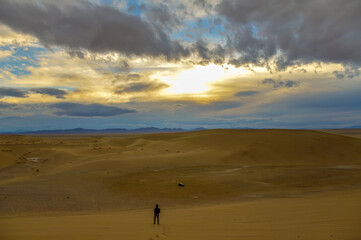 Fototapeta na wymiar Unidentified person standing alone in the sands of the Varzaneh sand dunes in Iran at sunset
