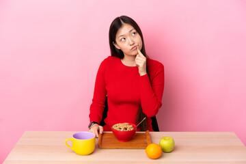 Young Chinese girl  having breakfast in a table having doubts while looking up