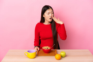 Young Chinese girl  having breakfast in a table yawning and covering wide open mouth with hand