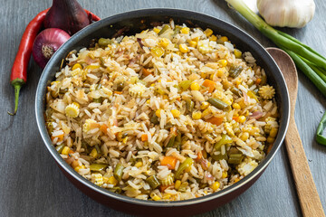 Fried rice with vegetables in a metal bowl on a wooden table with ingredients - simple oriental cuisine