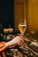 Woman holding a glass of rose champagne at a restaurant on bar counter.