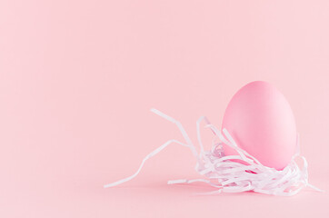 Gentle and girlish easter background - easter egg in white nest standing on pastel pink backdrop, copy space.